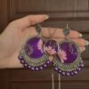 "Hand holding a pair of intricately designed silver and purple earrings with floral resin details, accompanied by a matching pendant necklace."