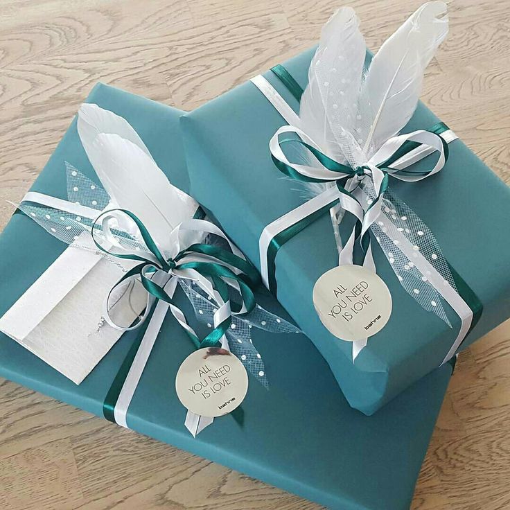 "Elegant teal gift boxes decorated with white feathers, ribbons, and a tag reading 'All You Need is Love'."