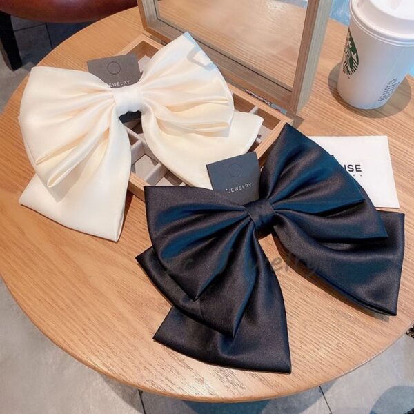 "Elegant black and white satin bows displayed on a wooden table with a jewelry box and a Starbucks cup in the background."