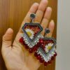 "Hand holding a pair of handcrafted silver and red resin earrings with embedded white flowers and dangling red beads."
